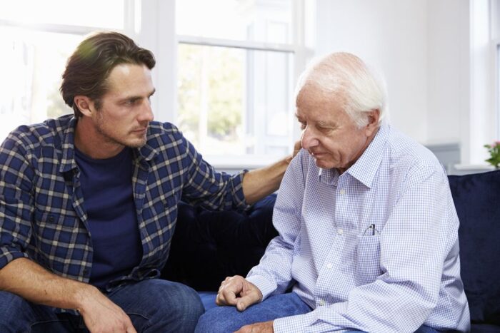 A concerned younger man consoling an older man, the victim of mail scams targeting seniors.